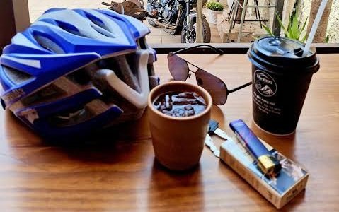 Iced coffee, sunglasses and a motorbike helmet on a café table by an open window