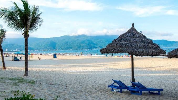 Thatched umbrella and blue sun loungers on My Khe Beach in Da Nang, with mountains across the bay